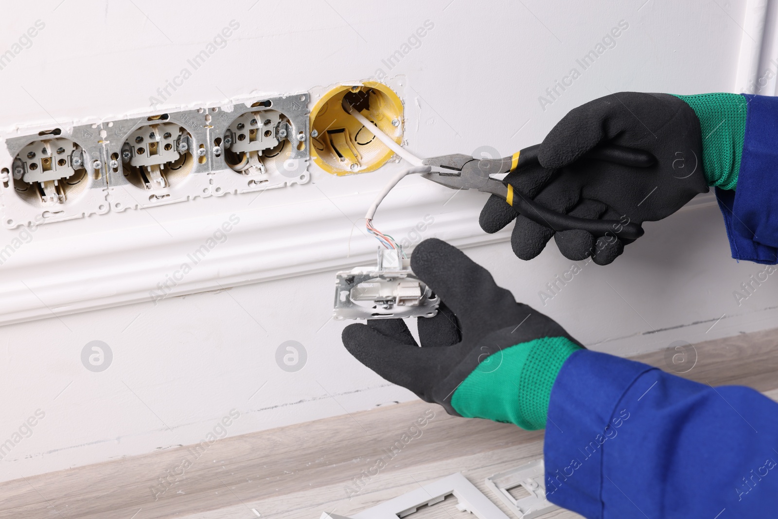 Photo of Professional repairman fixing power sockets with pliers indoors, closeup