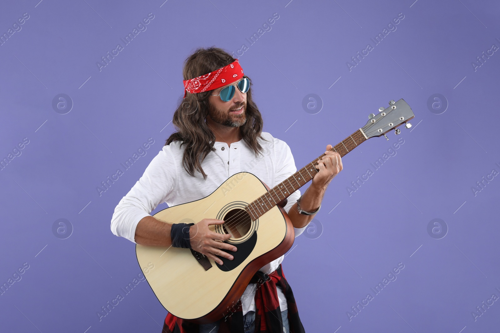 Photo of Stylish hippie man in sunglasses playing guitar on violet background