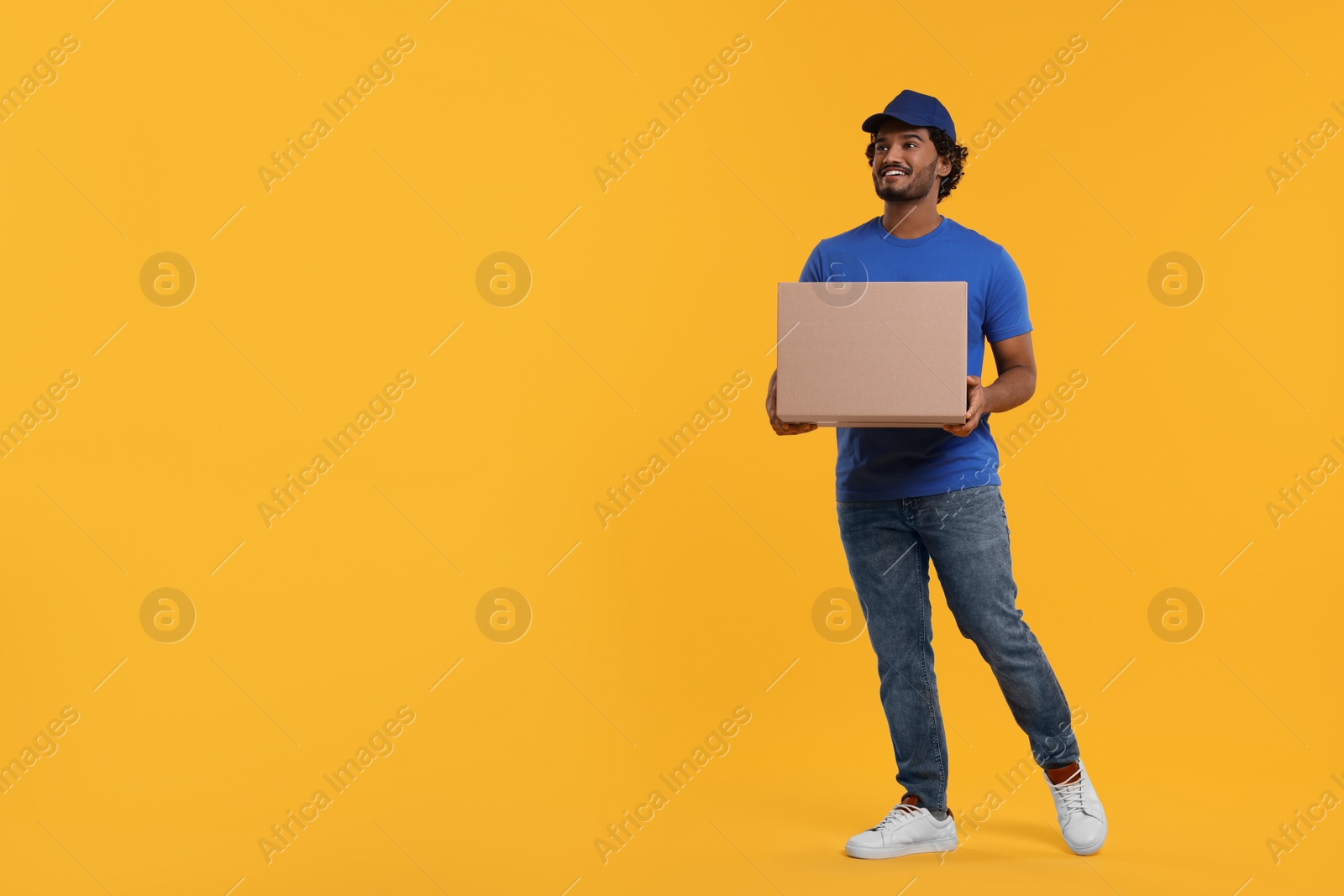 Photo of Happy courier with parcel on orange background, space for text