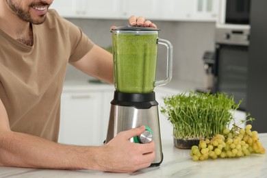 Photo of Happy man blending delicious smoothie at white table in kitchen, closeup