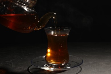 Photo of Pouring traditional Turkish tea from pot into glass on black table