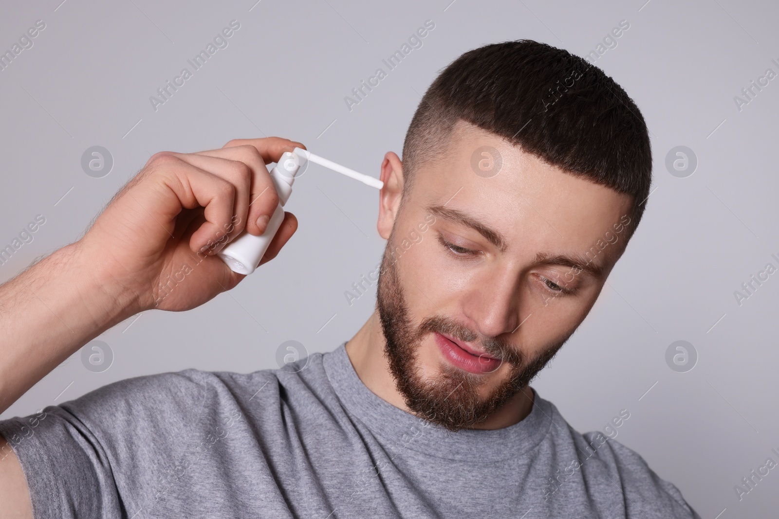 Photo of Man using ear spray on light grey background