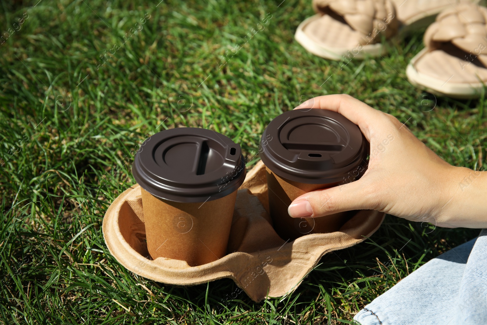 Photo of Woman holding takeaway cardboard coffee cups with plastic lids on green grass, closeup