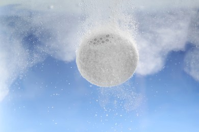 Photo of Effervescent pill dissolving in water on light blue background, closeup