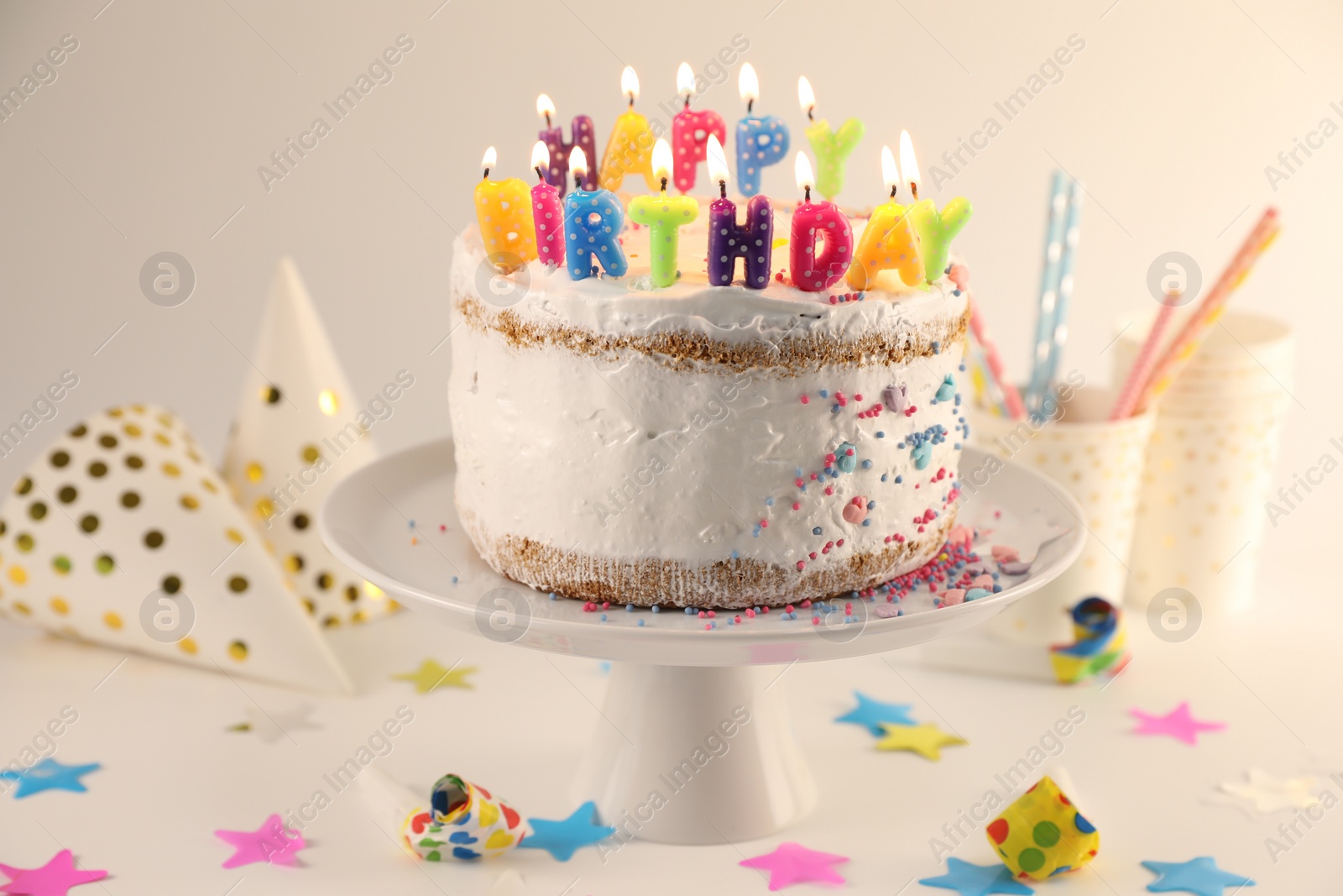 Photo of Tasty Birthday cake with burning candles and party decor on white table