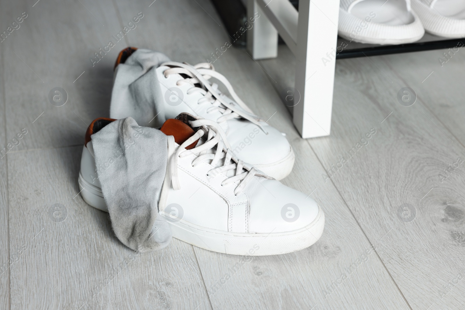 Photo of Sneakers with dirty socks on white wooden floor indoors