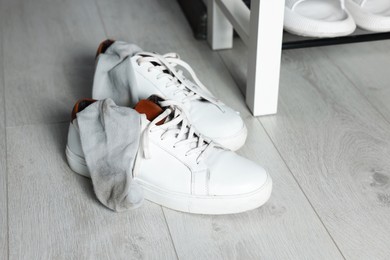 Photo of Sneakers with dirty socks on white wooden floor indoors