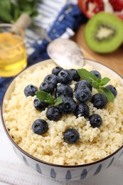 Bowl of tasty couscous with blueberries and mint on table, closeup