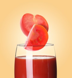 Image of Freshly made tomato juice on pale orange background. Cut tomato falling into glass