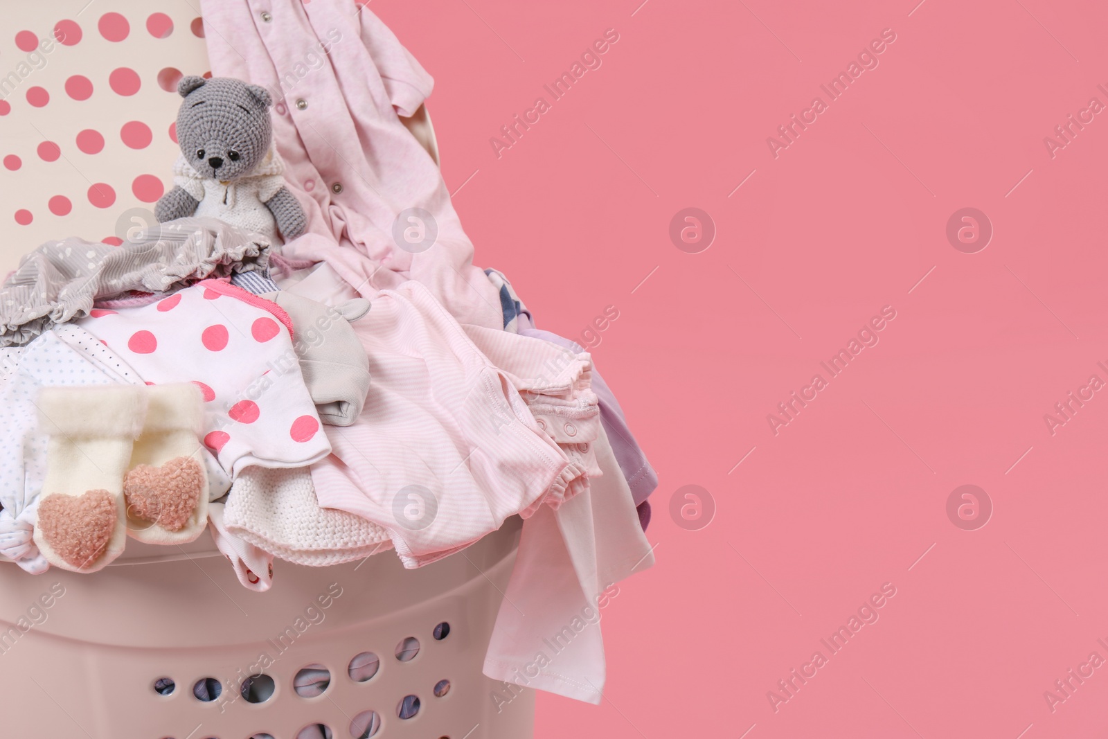 Photo of Laundry basket with baby clothes and soft toy on pink background, closeup. Space for text