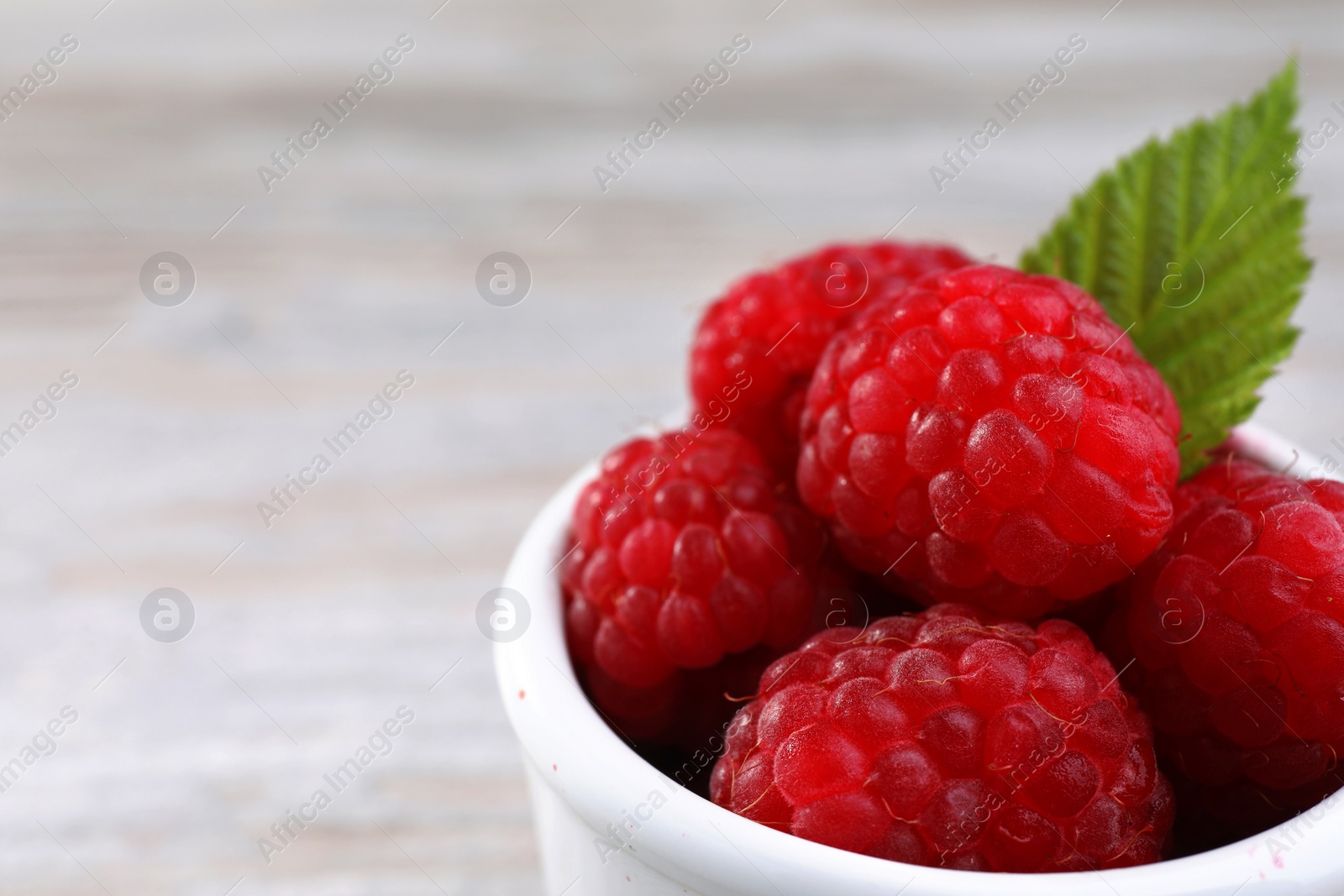 Photo of Tasty ripe raspberries and green leaf in white bowl, closeup. Space for text