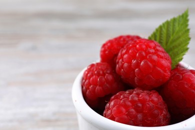 Tasty ripe raspberries and green leaf in white bowl, closeup. Space for text