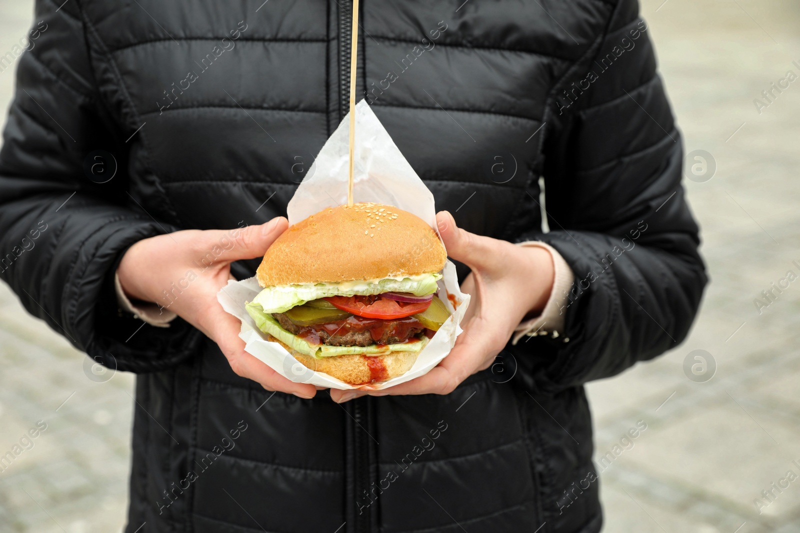 Photo of Woman holding fresh delicious burger outdoors, closeup. Street food