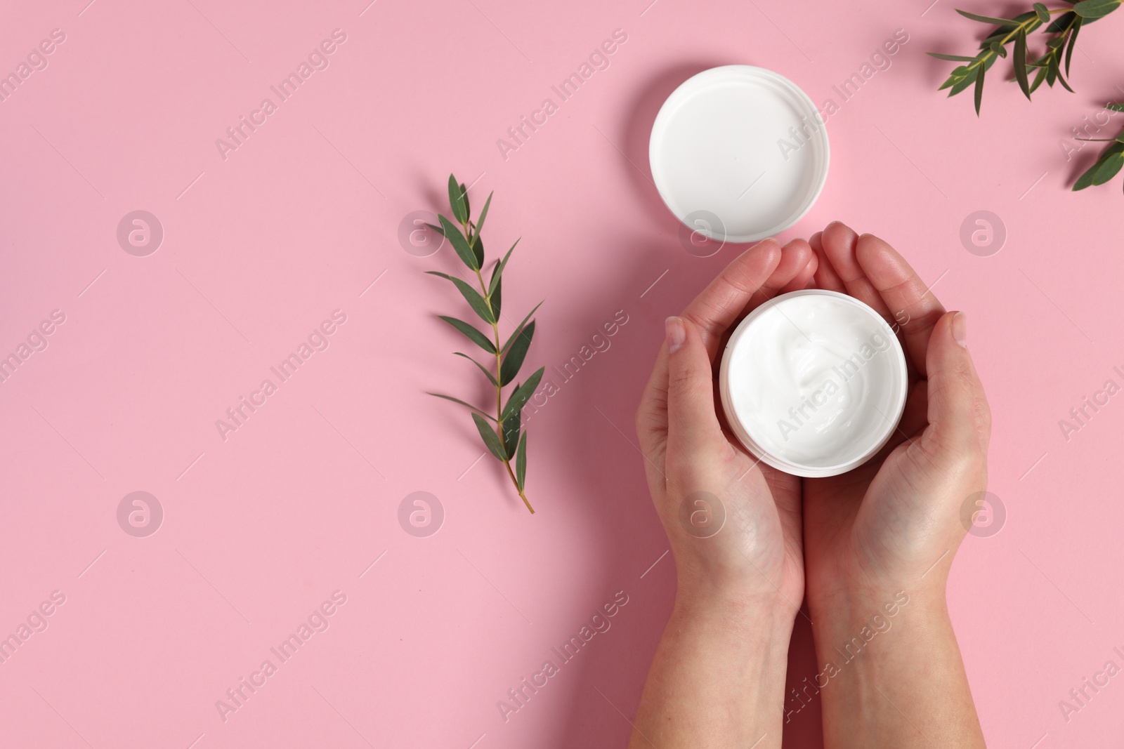 Photo of Woman with jar of hand cream and green twigs on pink background, top view. Space for text