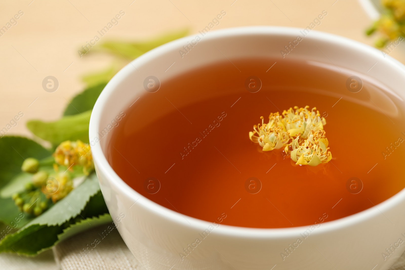 Photo of Cup of tea with linden blossom on table, closeup