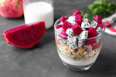 Photo of Glass of granola with different pitahayas, yogurt and mint on grey table, space for text