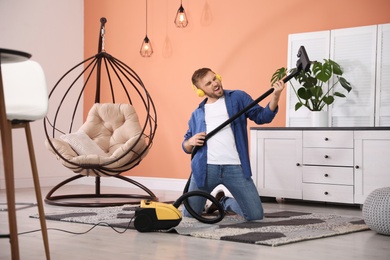 Young man having fun while vacuuming at home