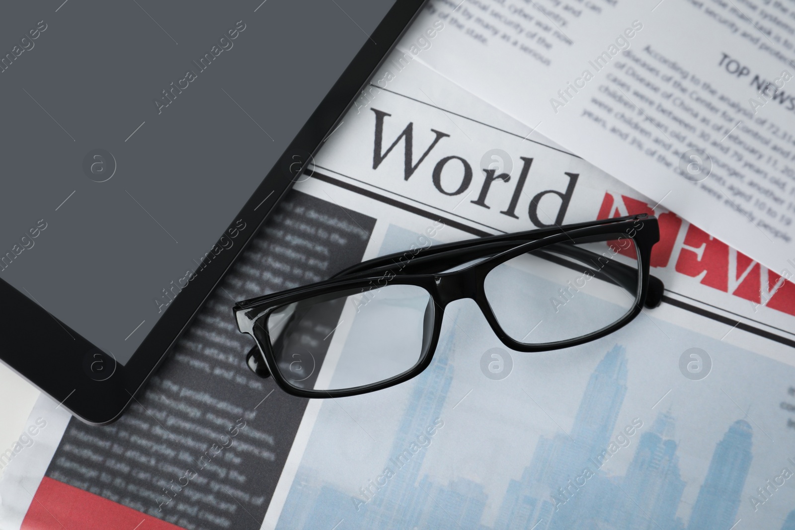 Photo of Glasses and tablet on newspapers, flat lay