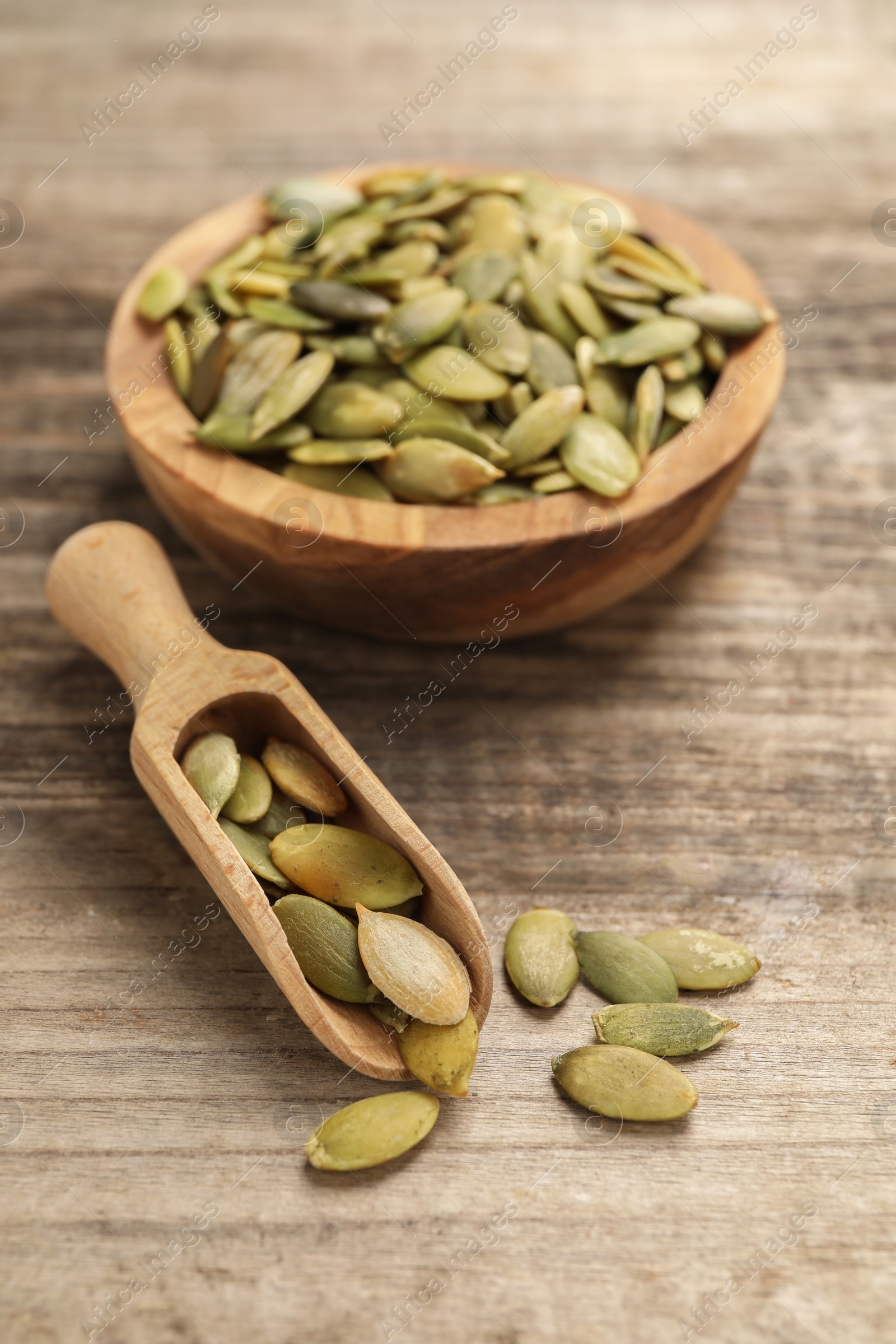 Photo of Bowl and scoop with peeled pumpkin seeds on wooden table