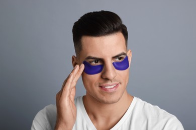 Photo of Man applying blue under eye patch on grey background