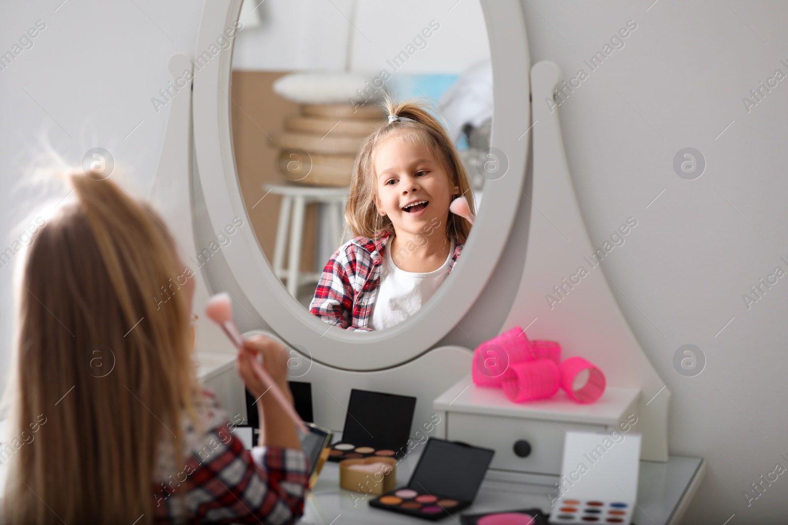 Photo of Adorable little girl applying makeup at dressing table indoors