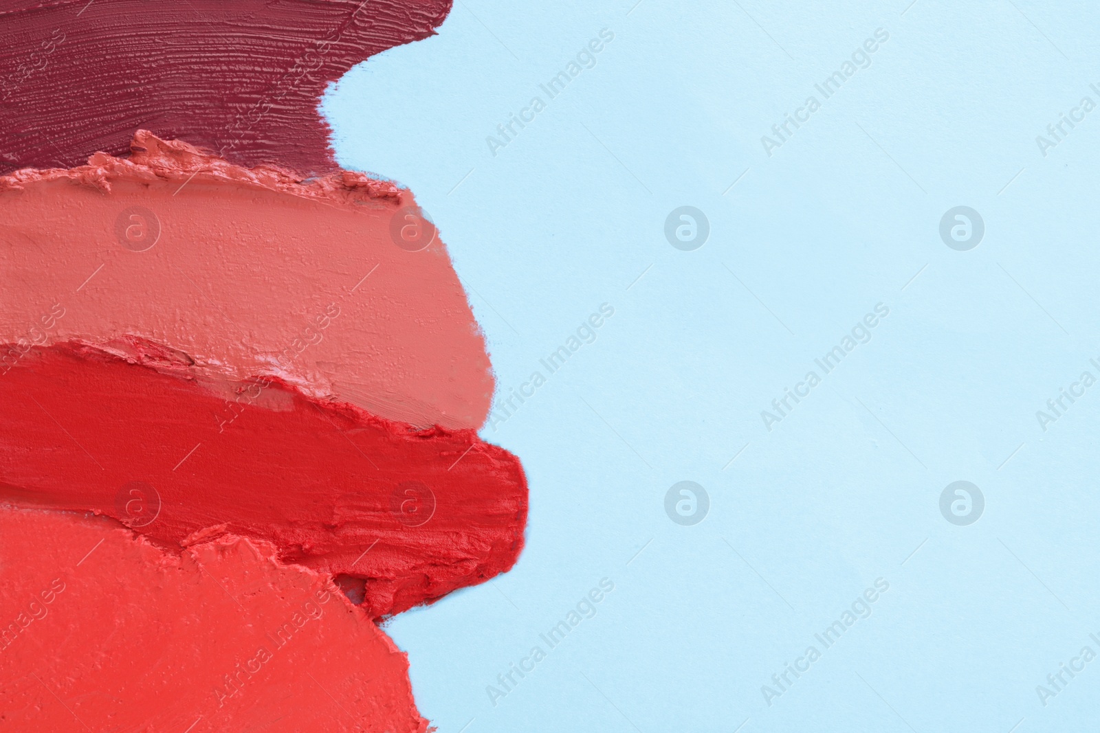 Photo of Smears of different beautiful lipsticks on light blue background, top view. Space for text