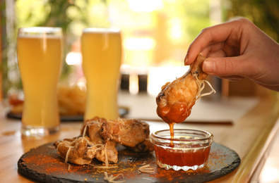 Photo of Woman dipping tasty BBQ wing into sauce at table, closeup