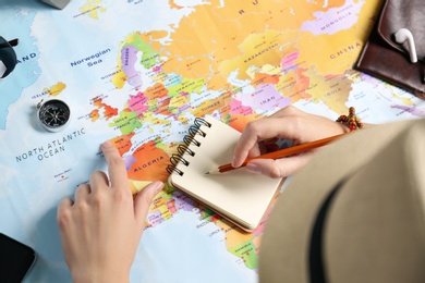 Photo of Woman using world map to plan trip at wooden table, closeup