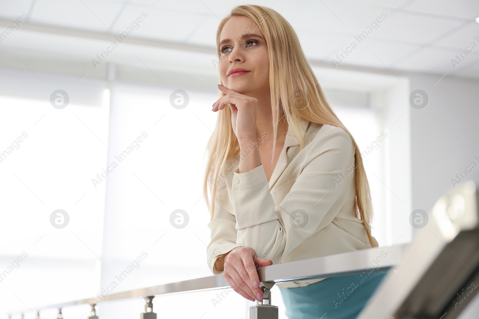 Photo of Young businesswoman leaning on railing in office, low angle view