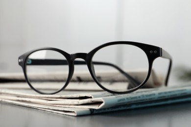 Stack of newspapers and glasses on grey table indoors, closeup