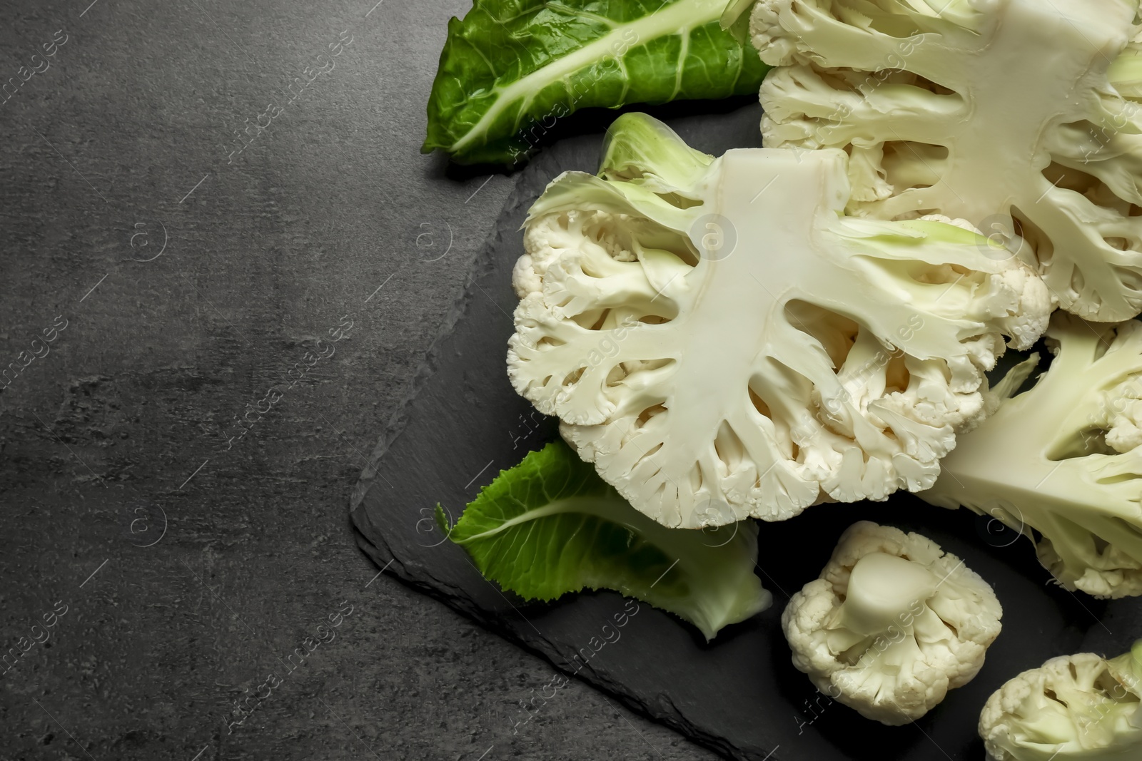 Photo of Cut fresh raw cauliflowers on black table, top view. Space for text
