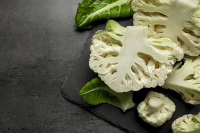 Photo of Cut fresh raw cauliflowers on black table, top view. Space for text