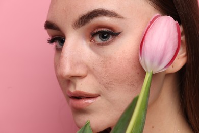 Beautiful woman with freckles and tulip on pink background, closeup