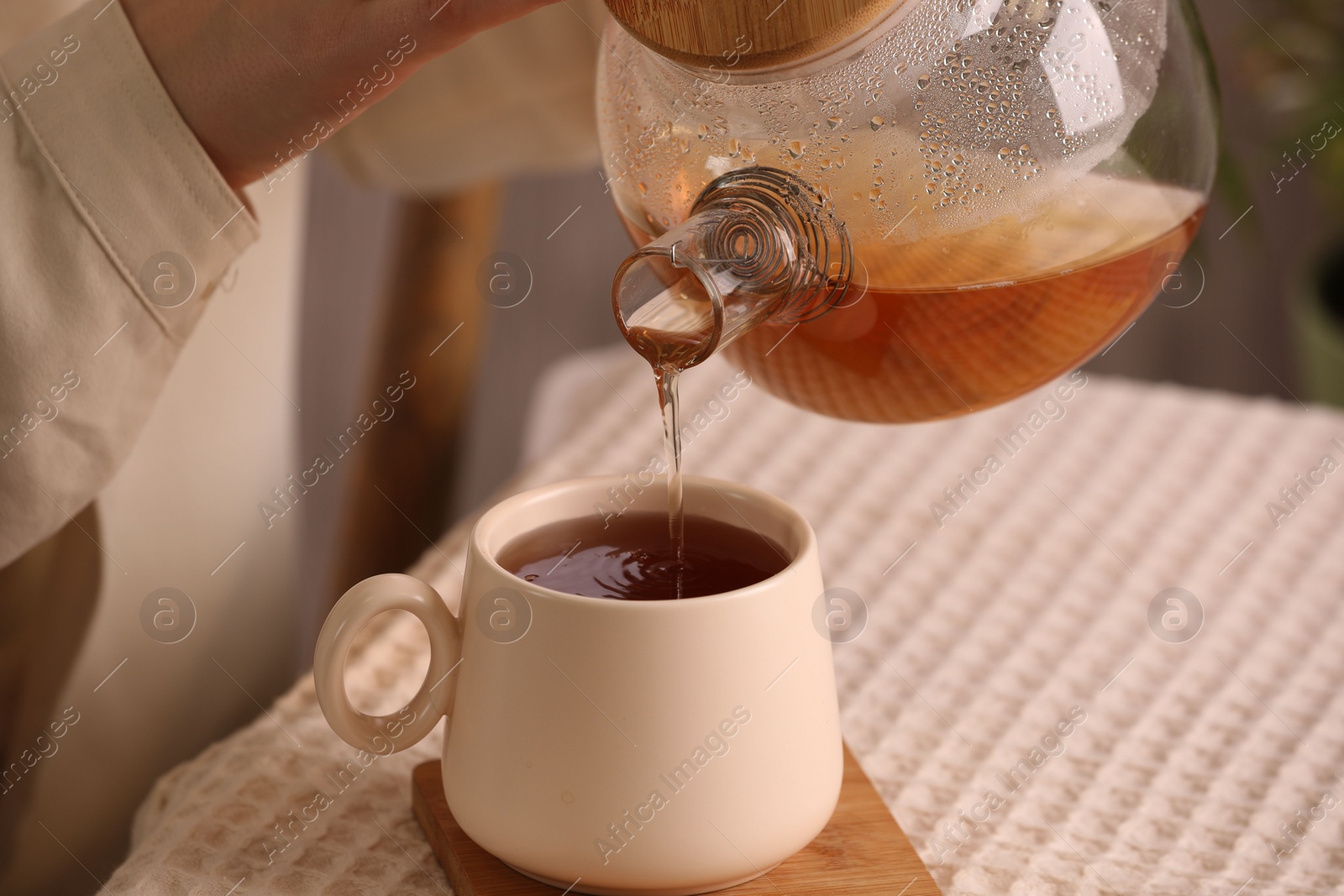Photo of Woman pouring aromatic tea into cup at table, closeup