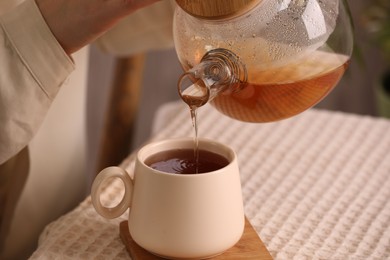 Woman pouring aromatic tea into cup at table, closeup