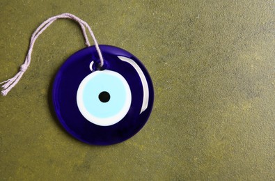 Photo of Evil eye amulet on olive textured table, top view. Space for text