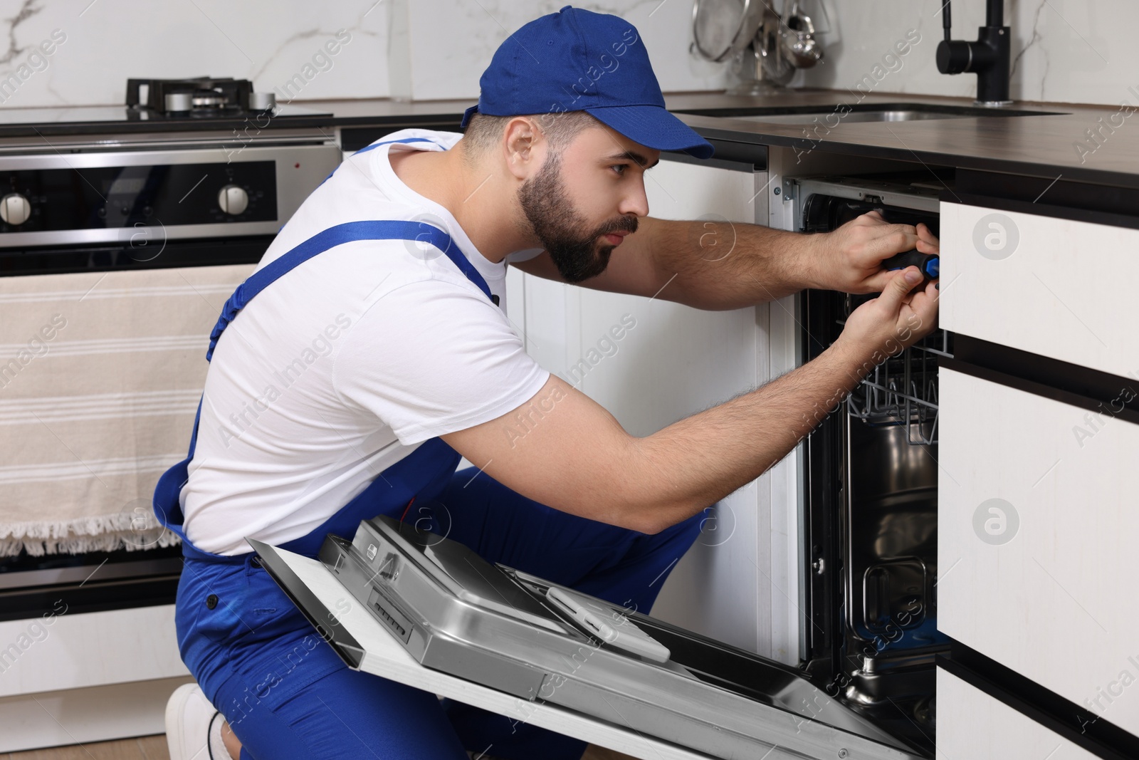 Photo of Serviceman repairing dishwasher with screwdriver in kitchen