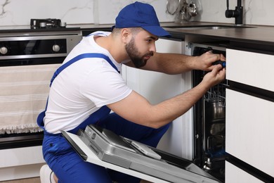 Serviceman repairing dishwasher with screwdriver in kitchen