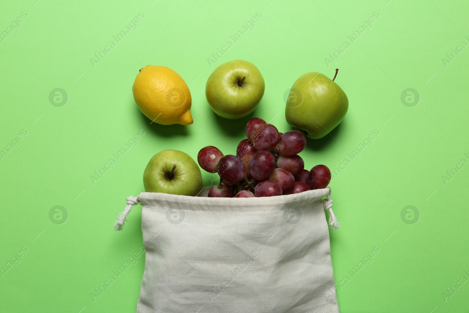 Photo of Cotton bag with juicy fruits on green background, flat lay