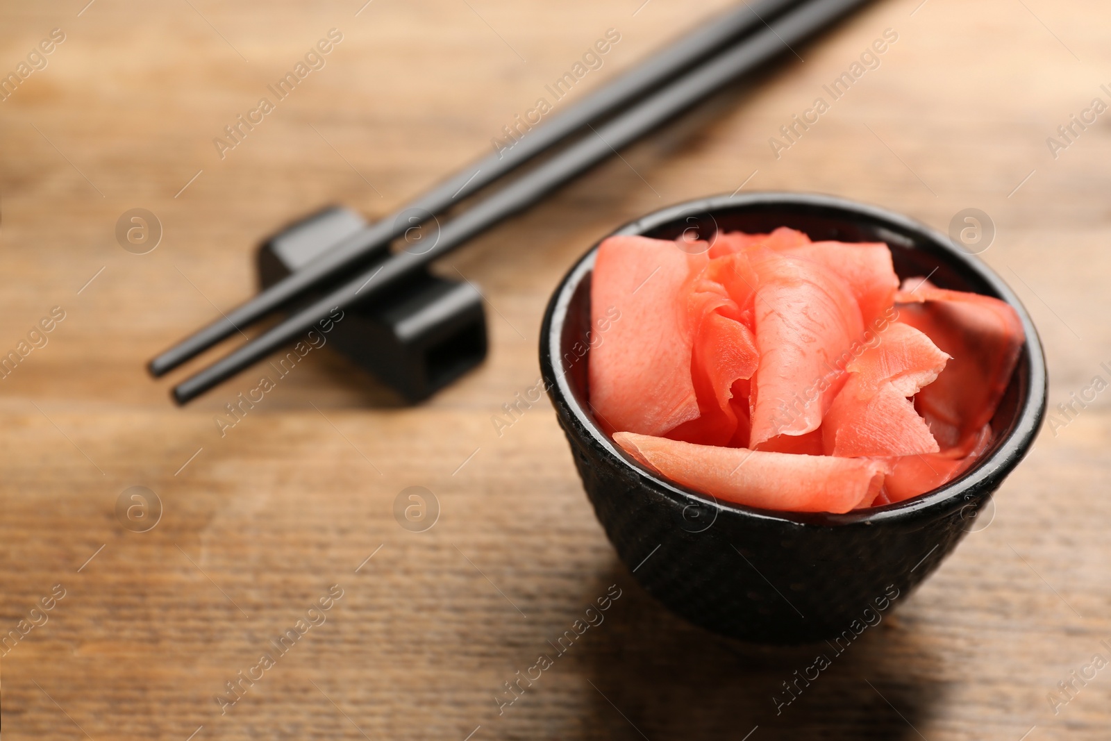 Photo of Spicy pickled ginger and chopsticks on wooden table, space for text