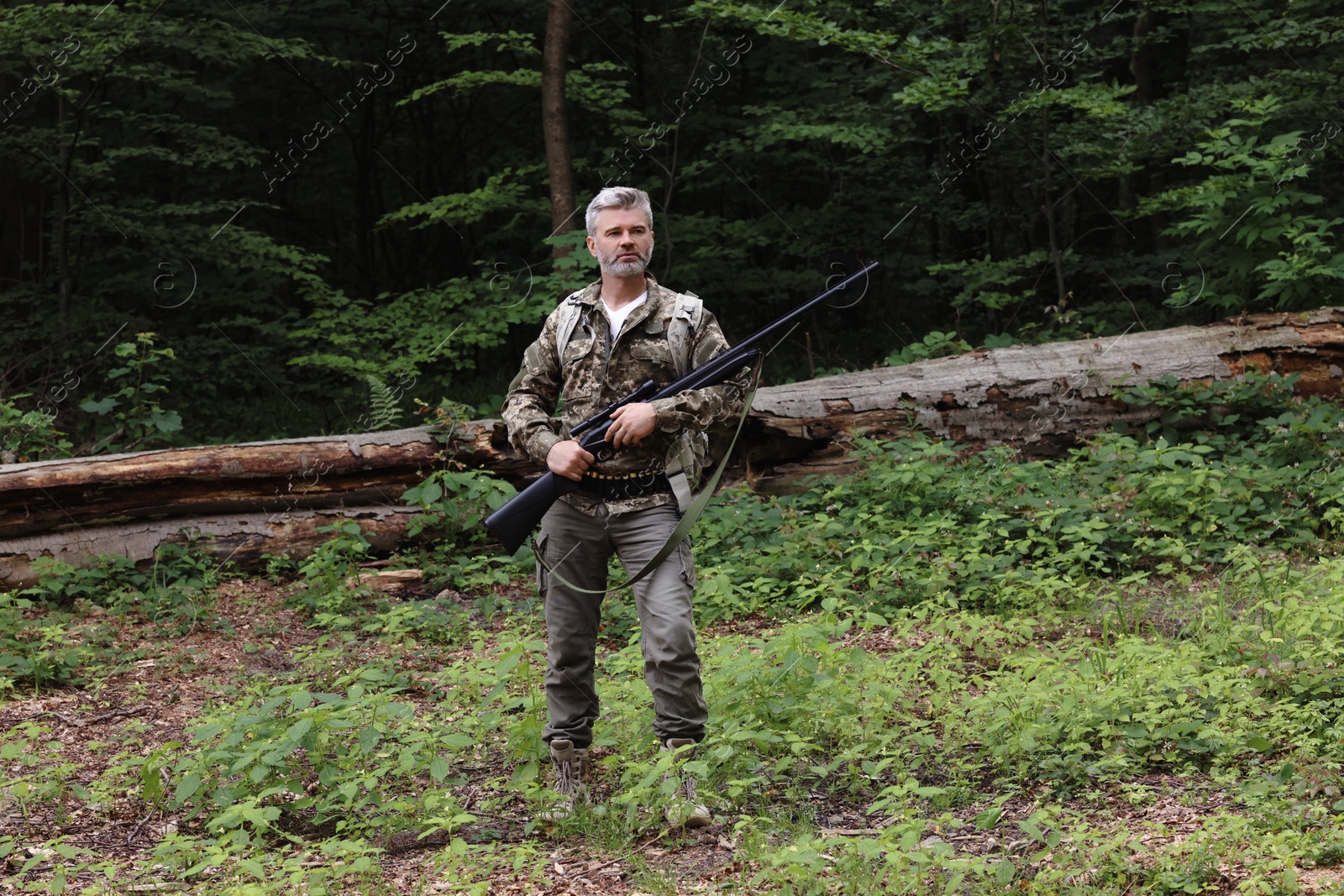 Photo of Man with hunting rifle and backpack wearing camouflage in forest