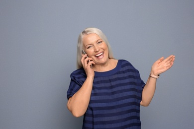 Mature woman talking on mobile phone against grey background