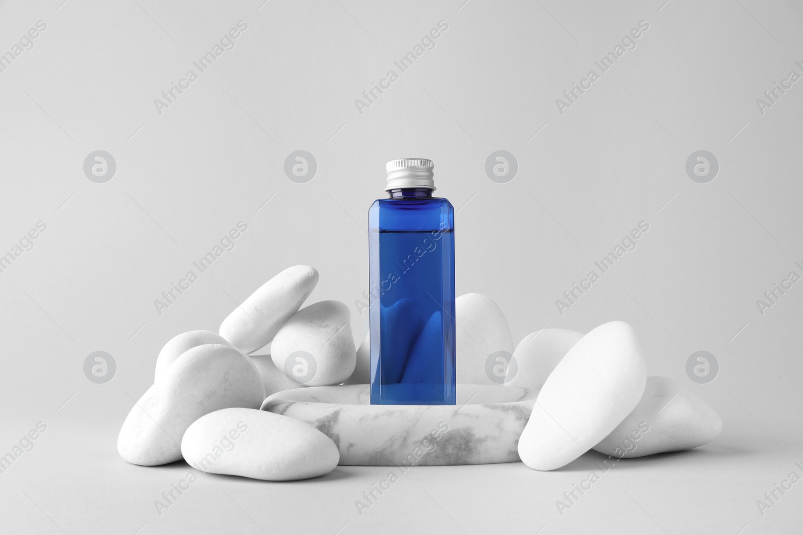 Photo of Bottle of cosmetic product and stones on light grey background