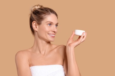 Woman with jar of body cream on beige background, space for text