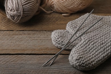 Photo of Soft colorful yarns, knitted socks and metal needles on wooden table, space for text