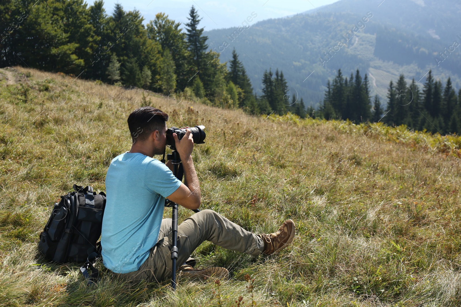 Photo of Man taking photo of mountain landscape with modern camera on tripod outdoors