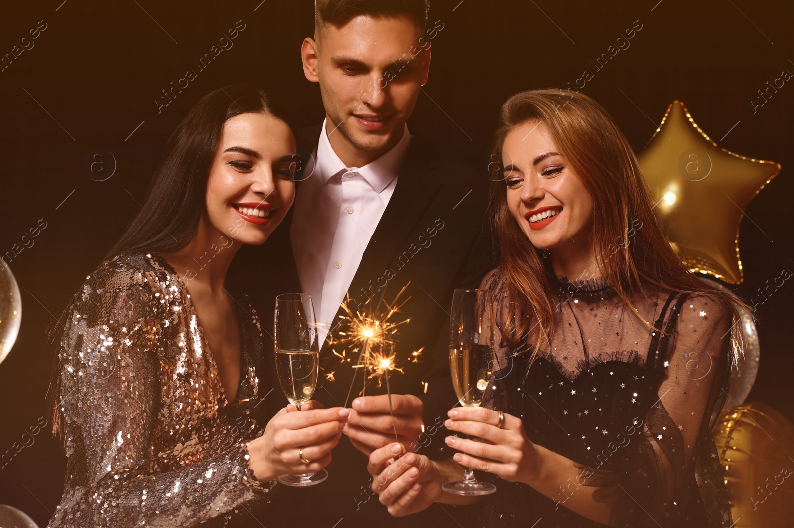 Photo of Happy friends with glasses of sparkling wine and sparklers celebrating New Year on black background