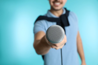 Young handsome man in casual clothes holding microphone on color background, closeup