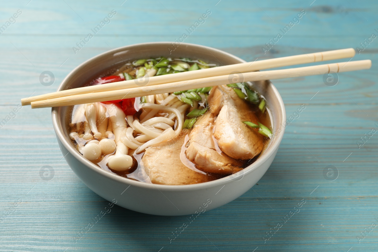 Photo of Delicious ramen with meat in bowl and chopsticks on light blue wooden table. Noodle soup