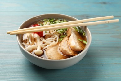 Delicious ramen with meat in bowl and chopsticks on light blue wooden table. Noodle soup